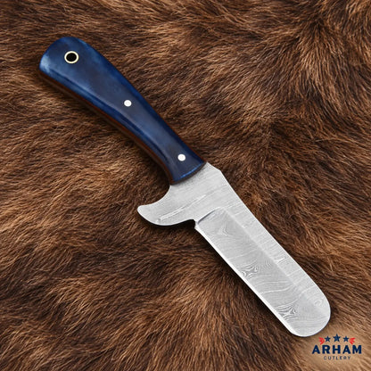 A fixed-blade knife with a patterned Damascus steel blade and a dark blue wooden handle, displayed diagonally on a brown fur background. The ARHAM Cutlery logo is visible in the bottom right corner.