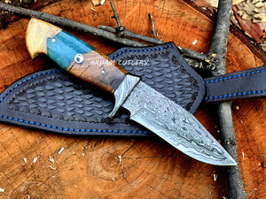 Hand-forged Damascus steel knife with epoxy and wood handle and custom leather sheath by Arham Cutlery, displayed on a wooden surface.