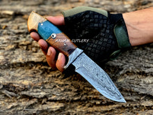 Cargar imagen en el visor de la galería, Hand-forged Damascus steel knife with epoxy and wood handle and custom leather sheath by Arham Cutlery, displayed on a wooden surface.
