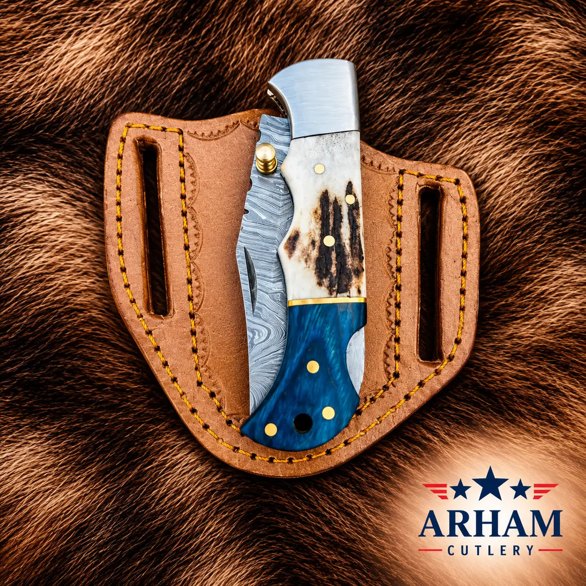 A folding pocket knife with a Damascus steel blade, a white and black bone handle, and a blue wood inlay, displayed in a brown leather sheath on a brown fur background. The ARHAM CUTLERY logo is visible in the bottom right corner.