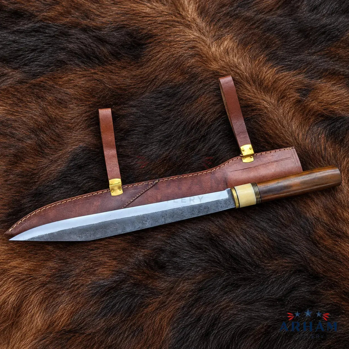A fixed-blade knife with a patterned steel blade, dark wood handle, and brass guard, displayed diagonally on its brown leather sheath over a brown fur background. The brand logo 'ARTHAM' is visible in the bottom right corner.