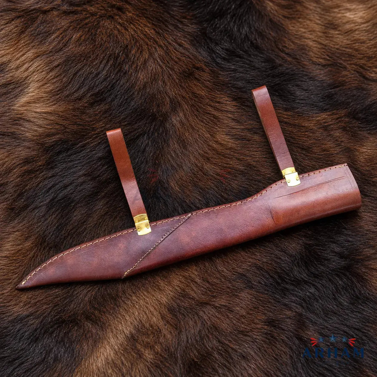 A brown leather knife sheath with brass grommets and two leather loops, laid diagonally on a dark brown fur background.