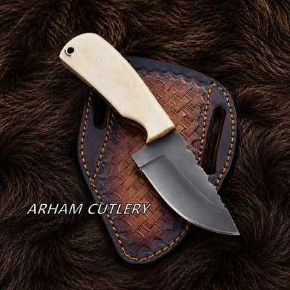 A fixed-blade knife with an ivory-colored handle and a dark steel blade, resting on a brown leather sheath over a dark brown fur background. The text 'ARHAM CUTLERY' is overlaid on the bottom left.
