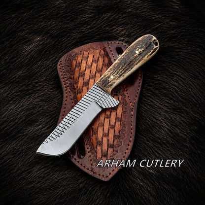 A fixed-blade knife with a patterned silver blade and a dark wood handle rests on a brown woven leather sheath over a dark fur background. The text 'ARHAM CUTLERY' is visible at the bottom right.