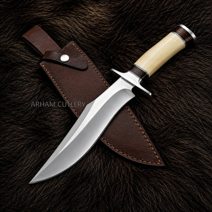 A fixed-blade hunting knife with a polished steel blade, cream-colored handle, and dark brown leather sheath, displayed diagonally on a dark brown fur background. The brand name 'ARHAM CUTLERY' is watermarked across the center.