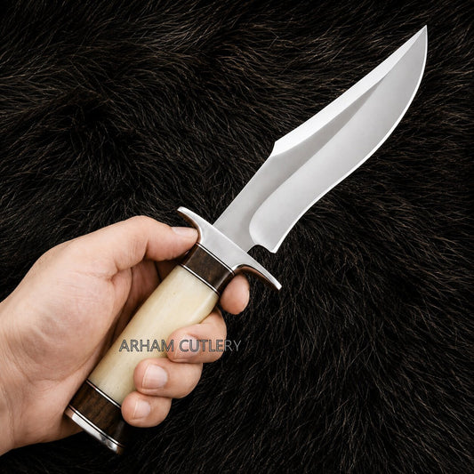 A hand holding a fixed-blade knife with a polished silver blade, a cream-colored bone handle, and dark brown wood accents, set against a black fur background. The brand name 'ARHAM CUTLERY' is watermarked across the center.