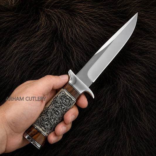 A hand holding a fixed-blade knife with a polished steel blade and an intricately carved brown and silver handle, set against a dark brown fur background. The watermark 'ARHAM CUTLERY' is visible on the left.