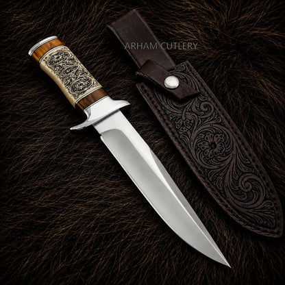 A fixed-blade knife with a polished silver blade, a carved wooden handle with silver engraved detailing, and a brown leather sheath, displayed on a dark brown fur background. The brand name 'ARHAM CUTLERY' is visible as a watermark.