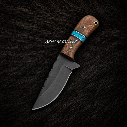 A fixed-blade knife with a dark gray steel blade and a brown wood handle featuring a turquoise inlay, displayed diagonally on a black textured fur background. The brand name 'ARHAM CUTLERY' is printed in white text across the handle.