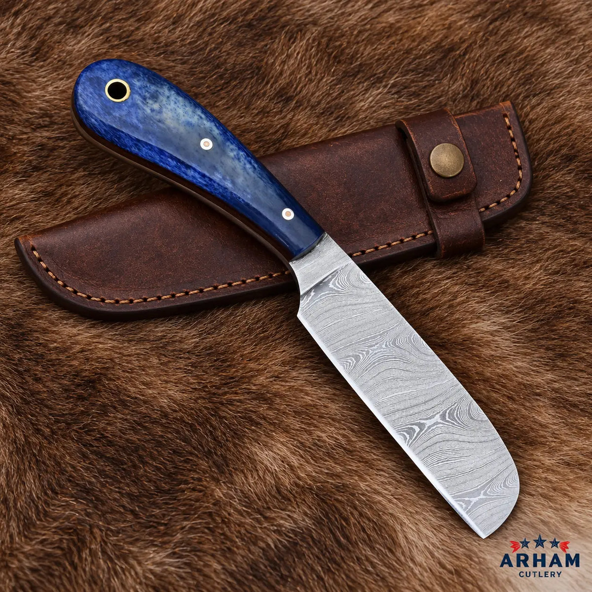 A fixed-blade knife with a patterned Damascus steel blade and a blue marbled handle, displayed diagonally on a brown leather sheath over a brown fur background. The ARHAM CUTLERY logo is visible in the bottom right corner.