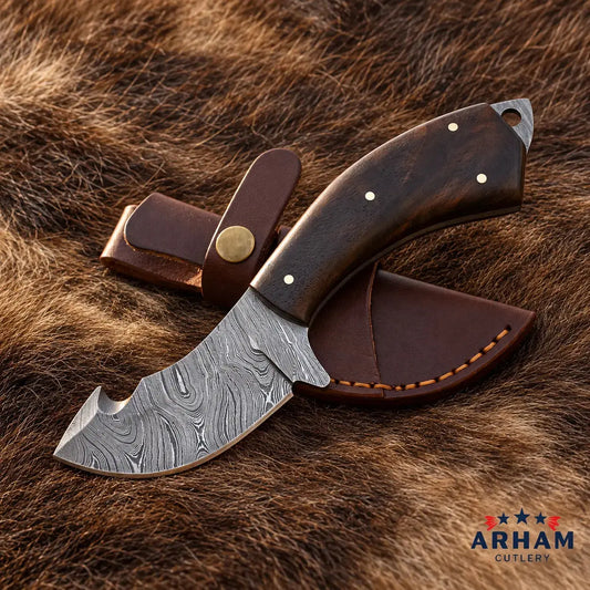 A fixed-blade knife with a patterned Damascus-style steel blade and a dark brown wooden handle, shown with a matching brown leather sheath on a brown fur background. The ARHAM CUTLERY logo appears in the bottom right corner.