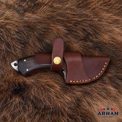 A fixed-blade knife with a dark wood handle and a brown leather sheath, displayed on a brown fur background. The sheath features a brass snap button and contrast stitching.