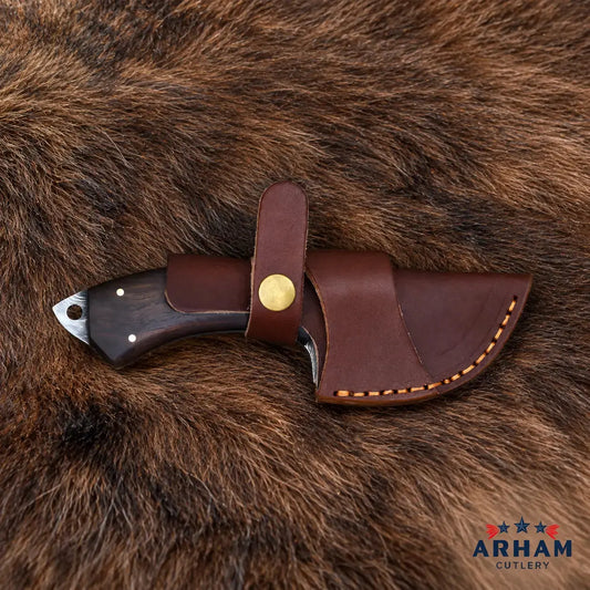 A fixed-blade knife with a dark wood handle and a brown leather sheath, displayed on a brown fur background. The sheath features a brass snap button and contrast stitching.