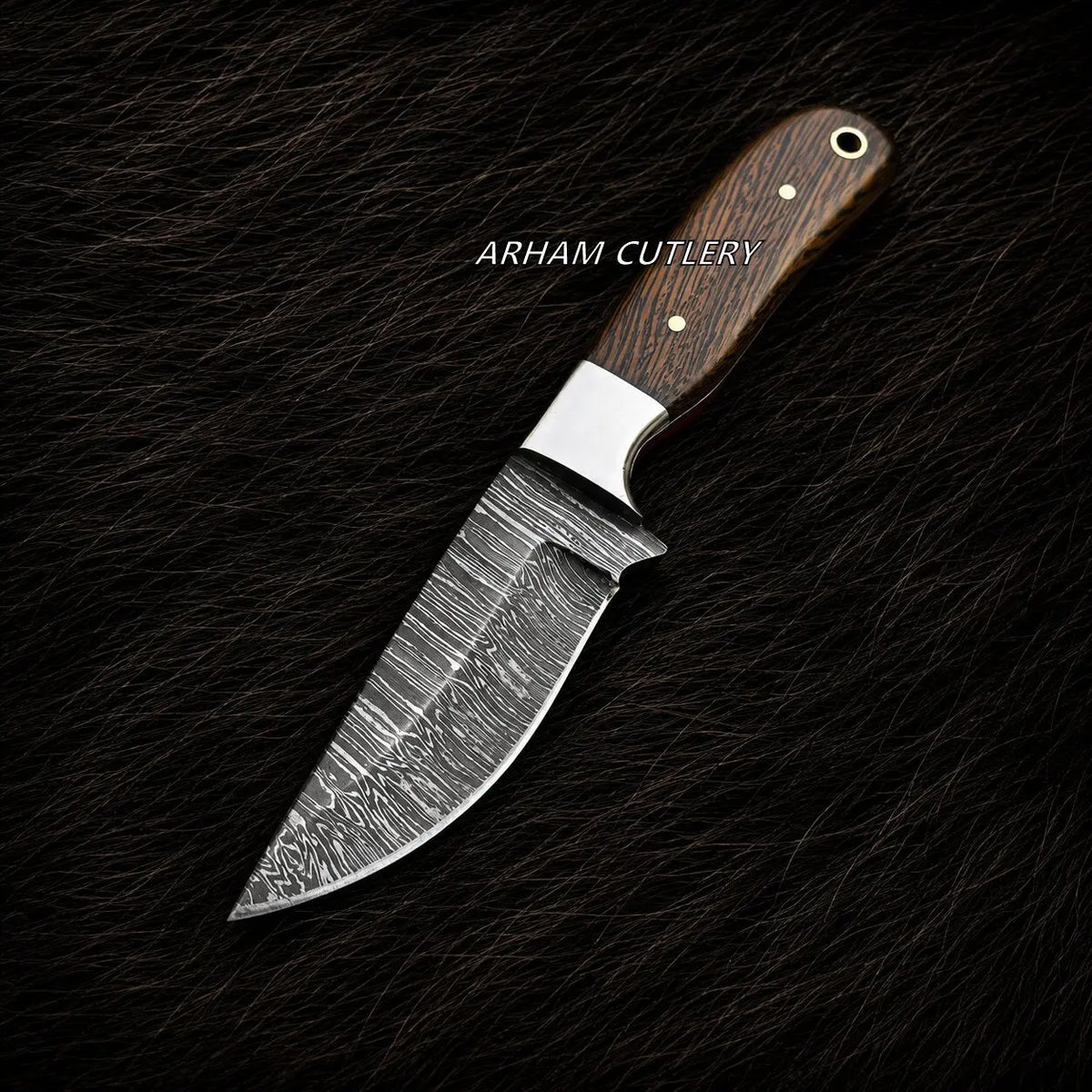 A fixed-blade knife with a patterned Damascus steel blade and a dark brown wood handle, displayed diagonally on a dark textured background. The brand name 'ARHAM CUTLERY' is printed in white text across the upper-middle section of the blade.