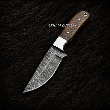A fixed-blade knife with a patterned Damascus steel blade and a dark brown wood handle, displayed diagonally on a dark textured background. The brand name 'ARHAM CUTLERY' is printed in white text across the upper-middle section of the blade.