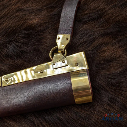 A close-up of a dark brown leather clutch or handbag with prominent polished gold-tone metal hardware, resting on a dark brown fur background. The brand name 'ARIAN COLLECTION' is visible as a watermark in the bottom right corner.
