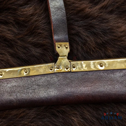 Close-up of a dark brown leather bag strap with a hammered brass clasp, resting on a dark brown fur surface. A small 'AOTAM' brand logo is visible in the bottom right corner.