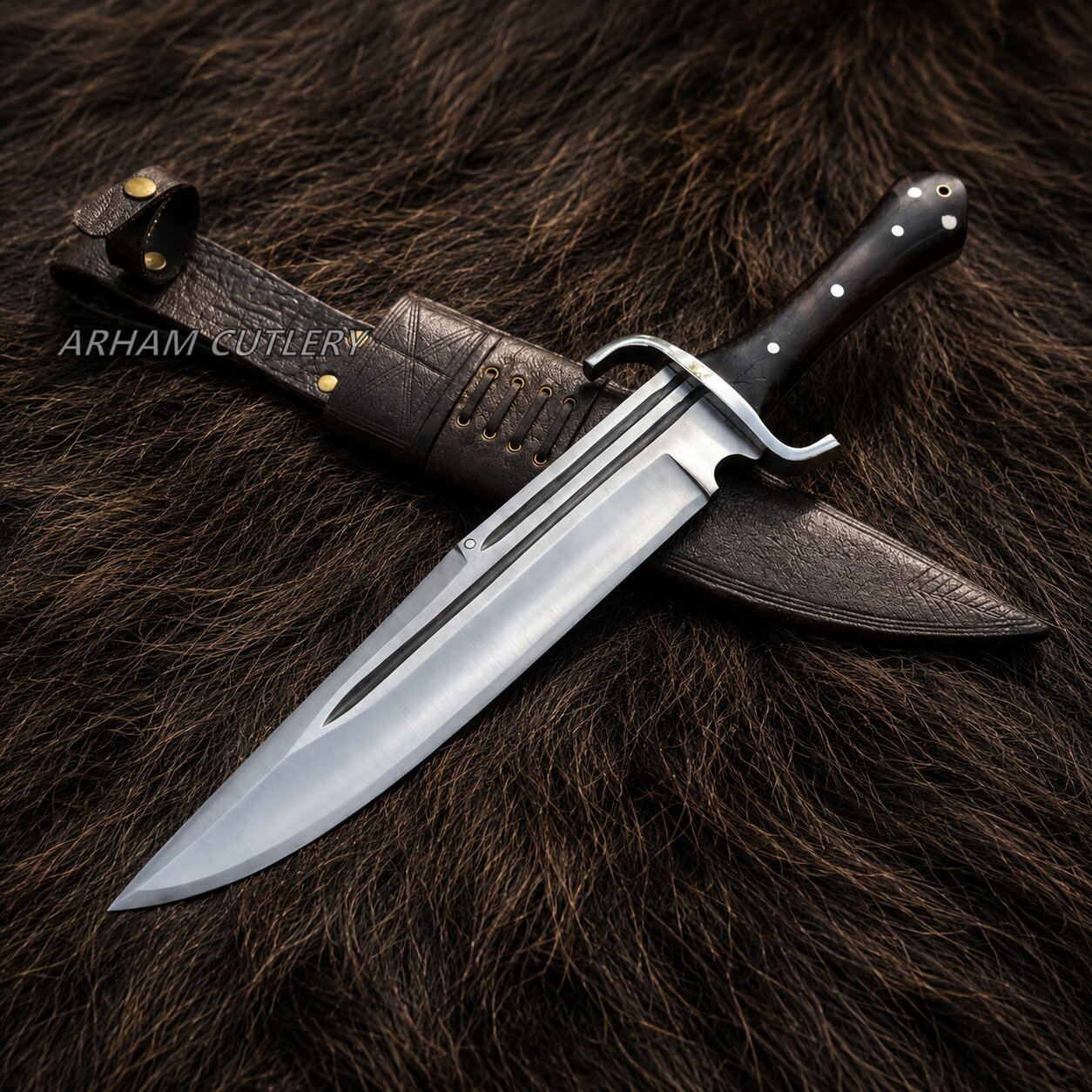 A fixed-blade knife with a polished silver blade, black handle, and brass guard, displayed diagonally with its dark brown leather sheath on a dark brown fur background. The brand name 'ARHAM COTLERY' is watermarked on the left.