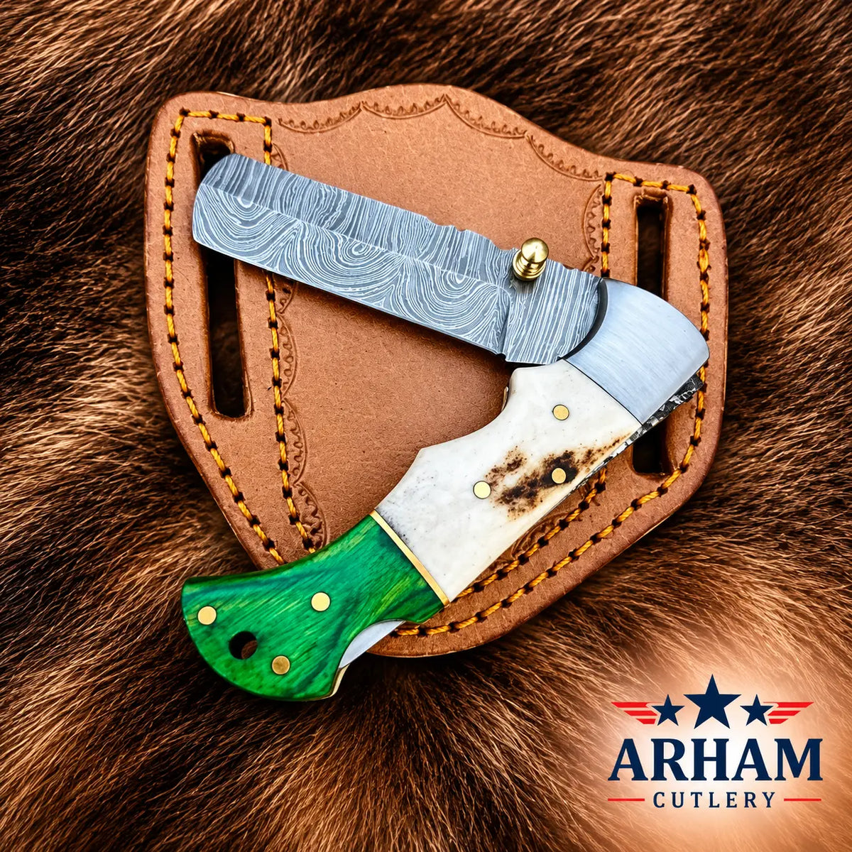 A folding pocket knife with a Damascus steel blade, white bone handle, and green contoured handle, resting on its brown leather sheath over a brown fur background. The Arham Cutlery logo is visible in the bottom right corner.