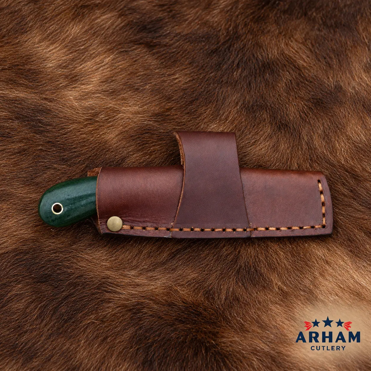 A brown leather knife sheath holding a knife with a dark green handle, laid flat on a brown fur surface. The Arham Cutlery logo is visible in the bottom right corner.