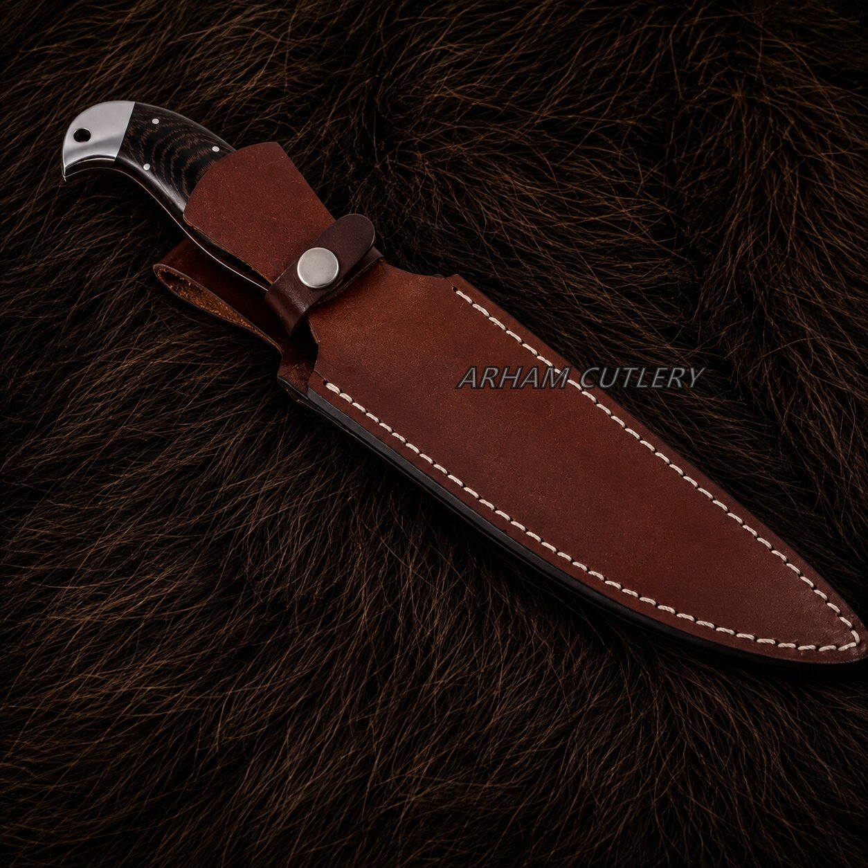 A brown leather knife sheath with white stitching, holding a partially serrated knife with a dark handle, displayed on a dark brown fur background. The brand name 'ARHAM CUTLERY' is watermarked across the center.