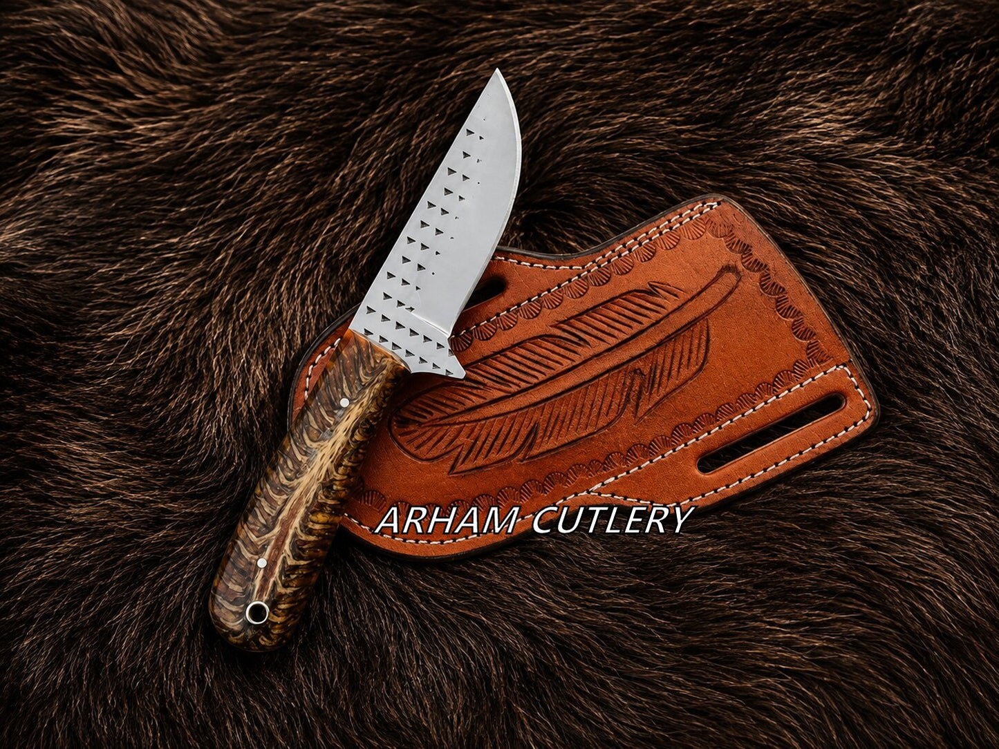 A fixed-blade knife with a patterned brown and gold handle and a silver blade, resting on a brown leather sheath with a feather design, all placed on a dark brown fur background. The text 'ARHAM CUTLERY' is overlaid across the center.