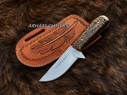 A fixed-blade knife with a silver steel blade and a carved dark wood handle, shown next to a brown leather sheath with an embossed feather design. The items are photographed on a brown fur surface, with the brand name 'ARHAM-CUTLERY' printed in white text across the center.