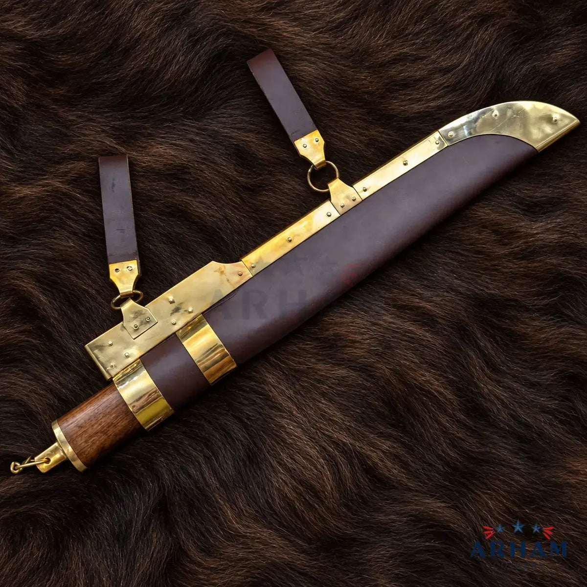 A decorative machete or ceremonial blade shown with its leather sheath and straps, placed on a dark brown fur background. The blade has brass-toned metal fittings, a brown leather sheath, and a wooden handle with brass accents.