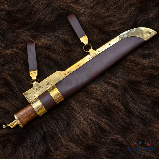 A decorative machete or ceremonial blade shown with its leather sheath and straps, placed on a dark brown fur background. The blade has brass-toned metal fittings, a brown leather sheath, and a wooden handle with brass accents.