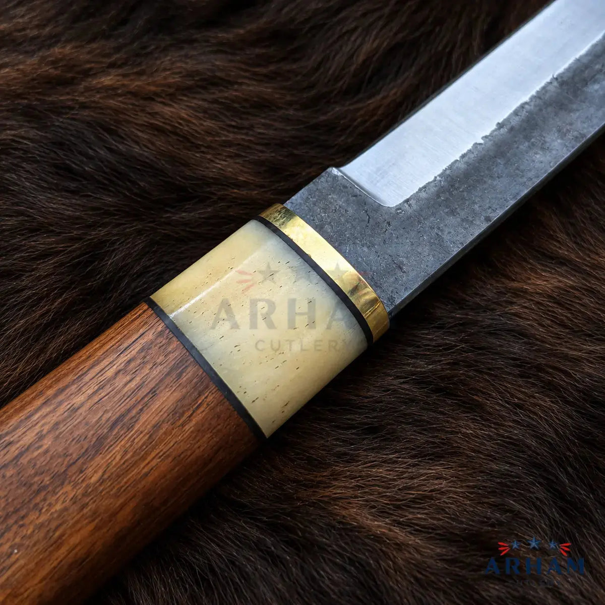 A close-up of a knife with a polished steel blade, a dark brown wood handle, and a cream-colored bone inlay with a gold band, resting on a dark brown fur background. The handle features a visible ARHA CUTLERY logo.