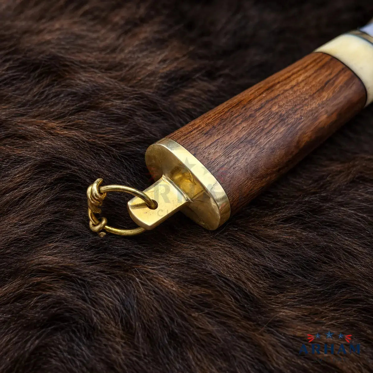 A close-up of a wooden sword hilt with brass fittings and a small hanging ring, resting on dark brown fur.