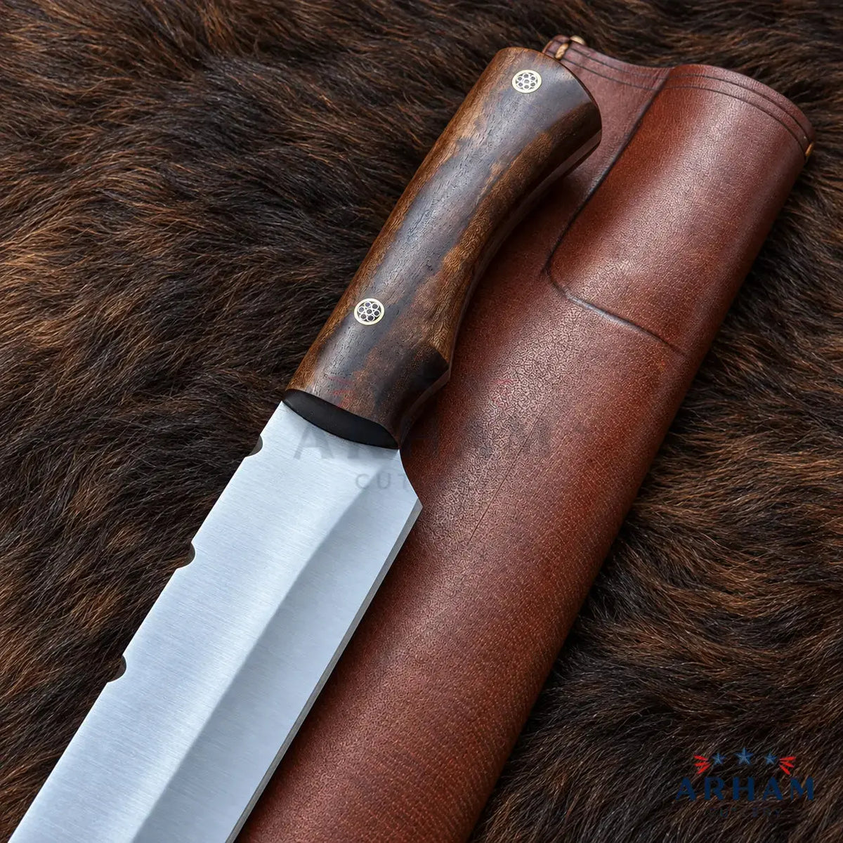A fixed-blade knife with a brushed silver blade and a dark brown wooden handle, shown alongside a brown leather sheath on a brown fur background. The brand name 'ADHAM' is visible as a watermark in the bottom right corner.