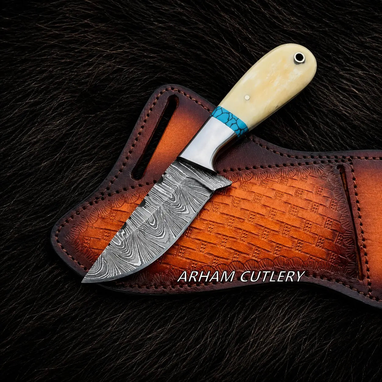 A fixed-blade knife with a patterned Damascus steel blade, a turquoise and silver wrapped bolster, and a cream-colored bone handle, resting on a brown embossed leather sheath over a dark fur background. The brand name 'ARHAM CUTLERY' is printed on the sheath.