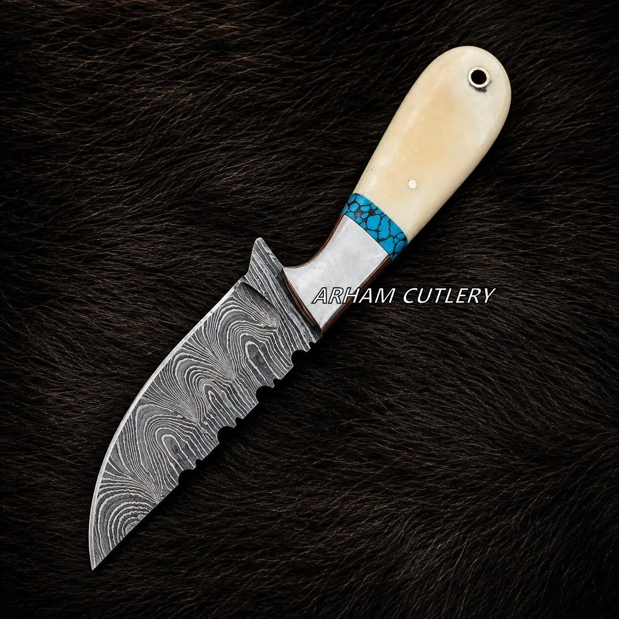 A custom fixed-blade knife with a Damascus steel blade, a turquoise and silver inlay, and a cream-colored bone handle, displayed on a dark brown fur background. The brand name 'ARHAM CUTLERY' is overlaid on the center of the image.