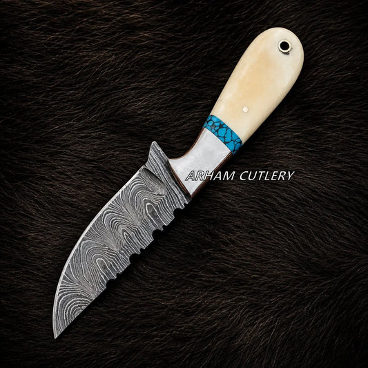 A custom fixed-blade knife with a Damascus steel blade, a turquoise and silver inlay, and a cream-colored bone handle, displayed on a dark brown fur background. The brand name 'ARHAM CUTLERY' is overlaid on the center of the image.
