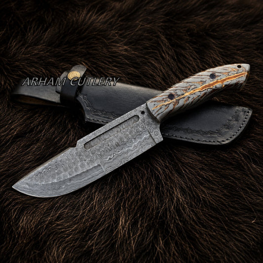 A fixed-blade knife with a patterned steel blade and a carved handle, shown with a black leather sheath on a dark brown fur background. The brand name 'ARHAM CUTLERY' is watermarked across the center.