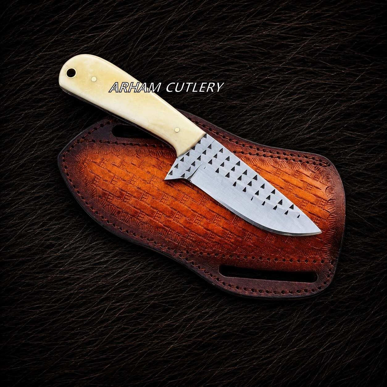 A fixed-blade knife with a cream-colored bone handle and a patterned silver blade, resting on a brown leather sheath over a dark textured fur background. The text 'ARHAM CUTLERY' is printed on the blade.