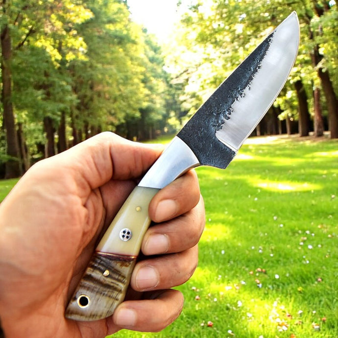 Handmade D2 steel knife with ram horn and camel bone handle shown in hand outdoors