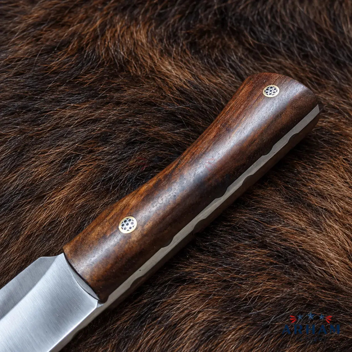 A close-up of a knife with a dark brown wooden handle and a satin-finished steel blade, placed diagonally on a brown fur surface. The handle has two small circular metal rivets.