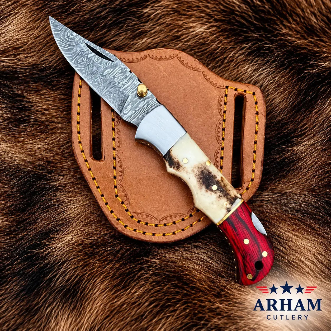 A custom handcrafted knife with a Damascus steel blade, bone handle, and red wood handle, resting on its brown leather sheath over a brown fur background. The ARHAM CUTLERY logo is visible in the bottom right corner.