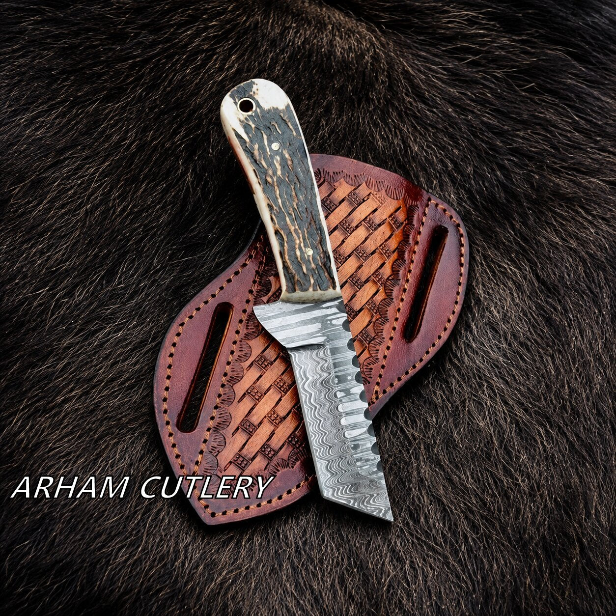 A fixed-blade knife with a patterned steel blade and a dark, marbled handle rests on a brown leather sheath over dark fur. The text 'ARHAM CUTLERY' is visible in the lower-left corner.