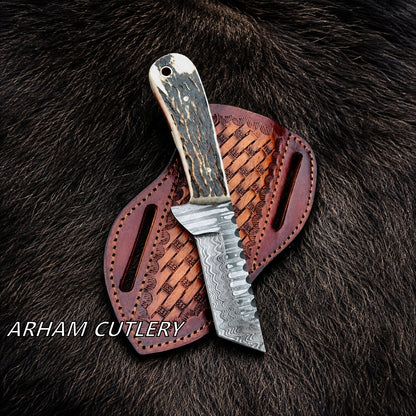 A fixed-blade knife with a patterned steel blade and a dark, marbled handle rests on a brown leather sheath over dark fur. The text 'ARHAM CUTLERY' is visible in the lower-left corner.