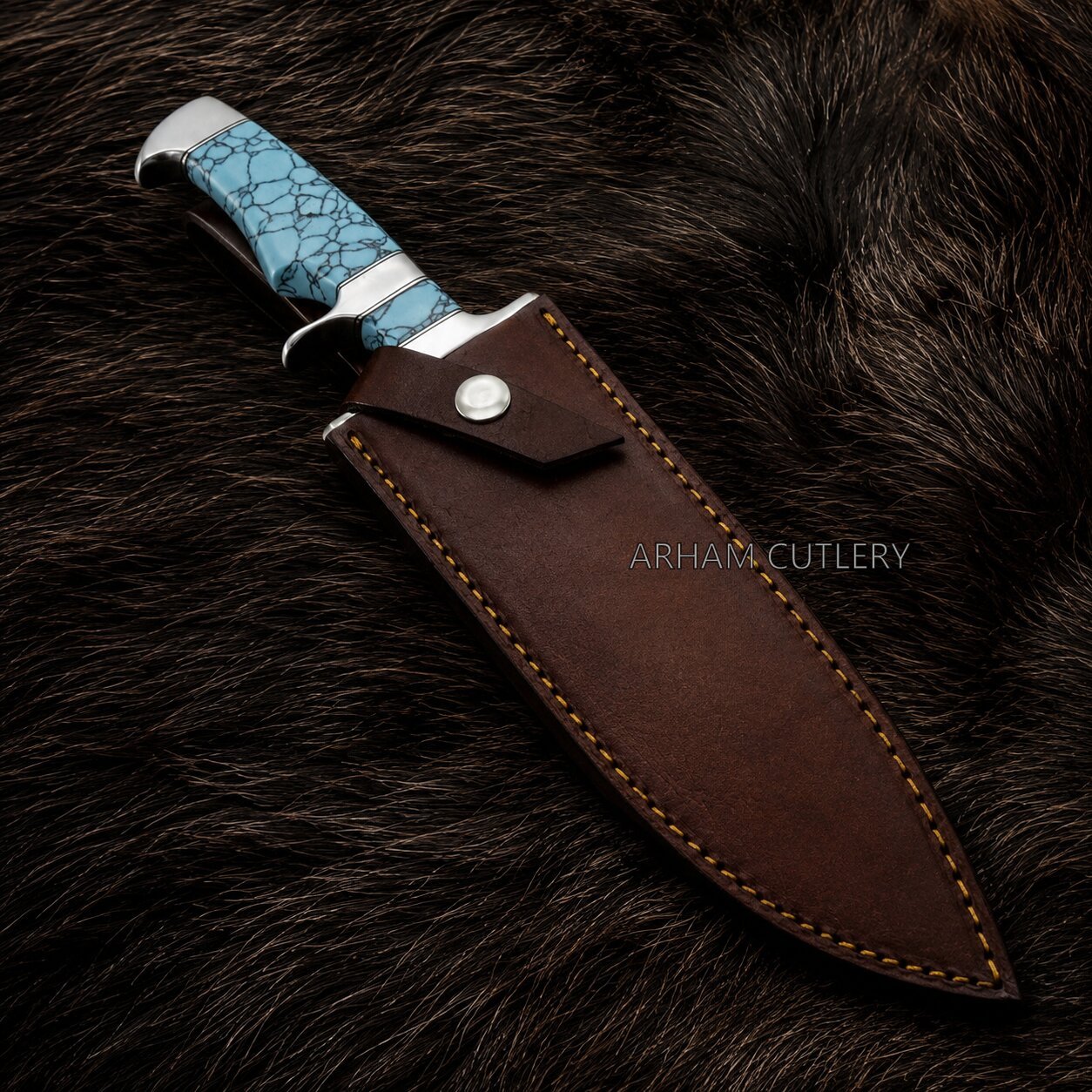 A fixed-blade knife with a textured turquoise blue handle and silver bolster, shown partially sheathed in a dark brown leather sheath with tan stitching, placed on a dark brown fur background. The brand name 'ARHAM CUTLERY' is watermarked on the sheath.
