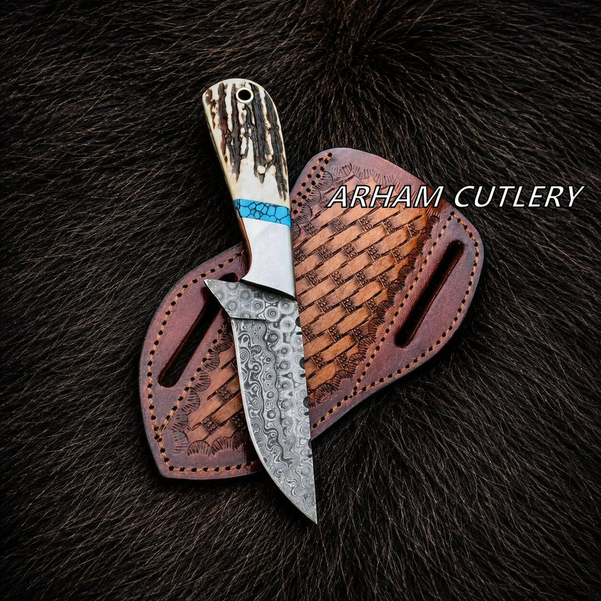 A fixed-blade knife with a patterned steel blade and a carved handle, displayed on top of a brown leather sheath against a dark fur background. The text 'ARHAM CUTLERY' is visible on the right side.