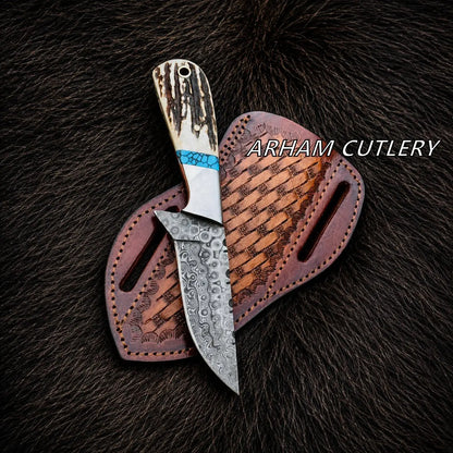 A fixed-blade knife with a patterned steel blade and a carved handle, displayed on top of a brown leather sheath against a dark fur background. The text 'ARHAM CUTLERY' is visible on the right side.
