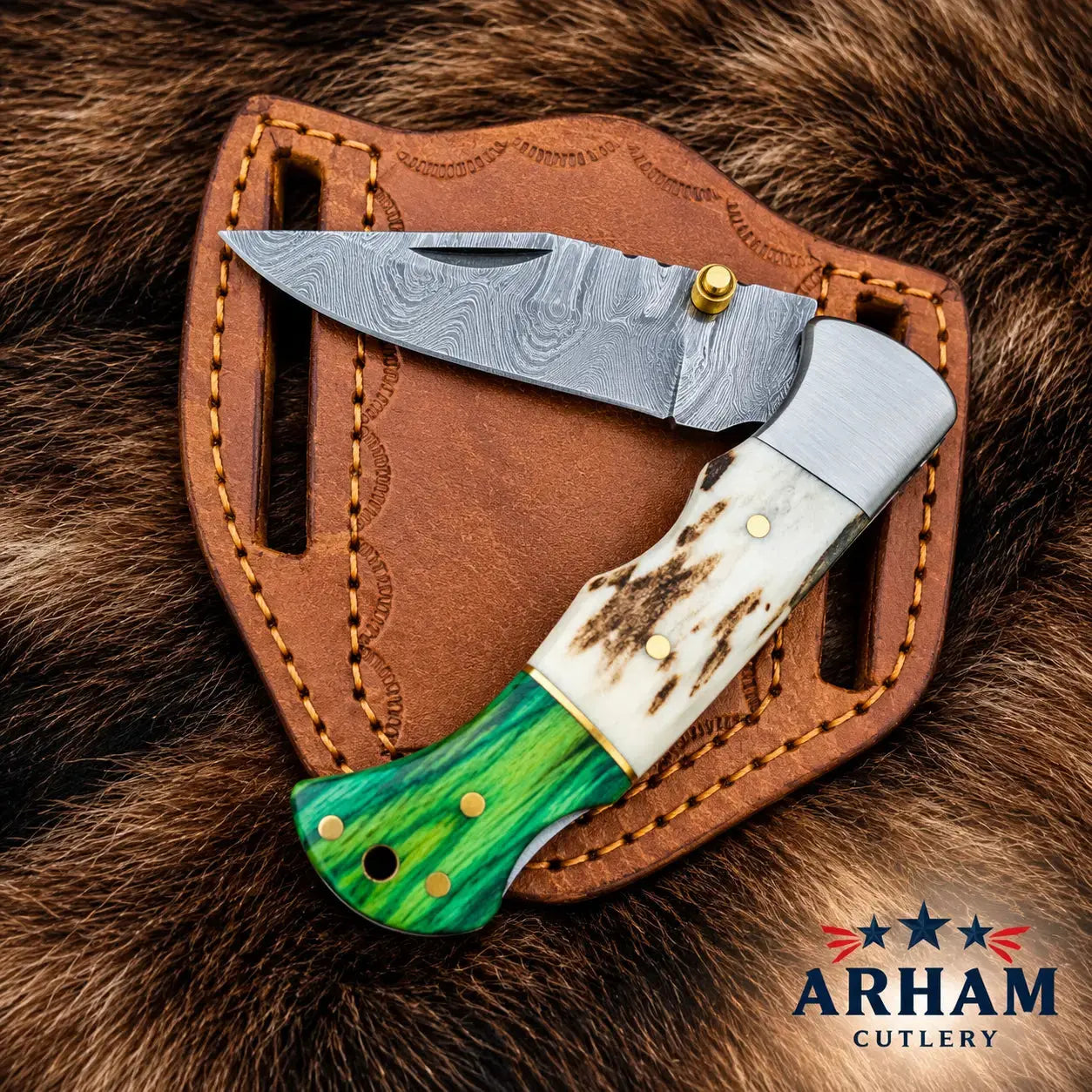 A folding pocket knife with a patterned steel blade, a white bone handle, and a green inlay handle, displayed on a brown leather sheath over a brown fur background. The ARHAM CUTLERY logo is visible in the bottom right corner.