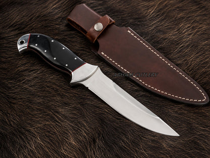A fixed-blade knife with a silver blade and black handle with silver rivets, displayed next to its brown leather sheath on a dark brown fur background. A faint watermark 'ARSHAD CUTLERY' is visible across the center.
