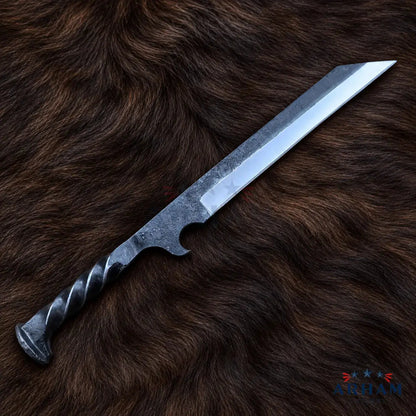 A large fixed-blade knife with a textured dark gray handle and a silver-gray steel blade, displayed diagonally on a brown fur background. The brand logo 'Artem Knife Co.