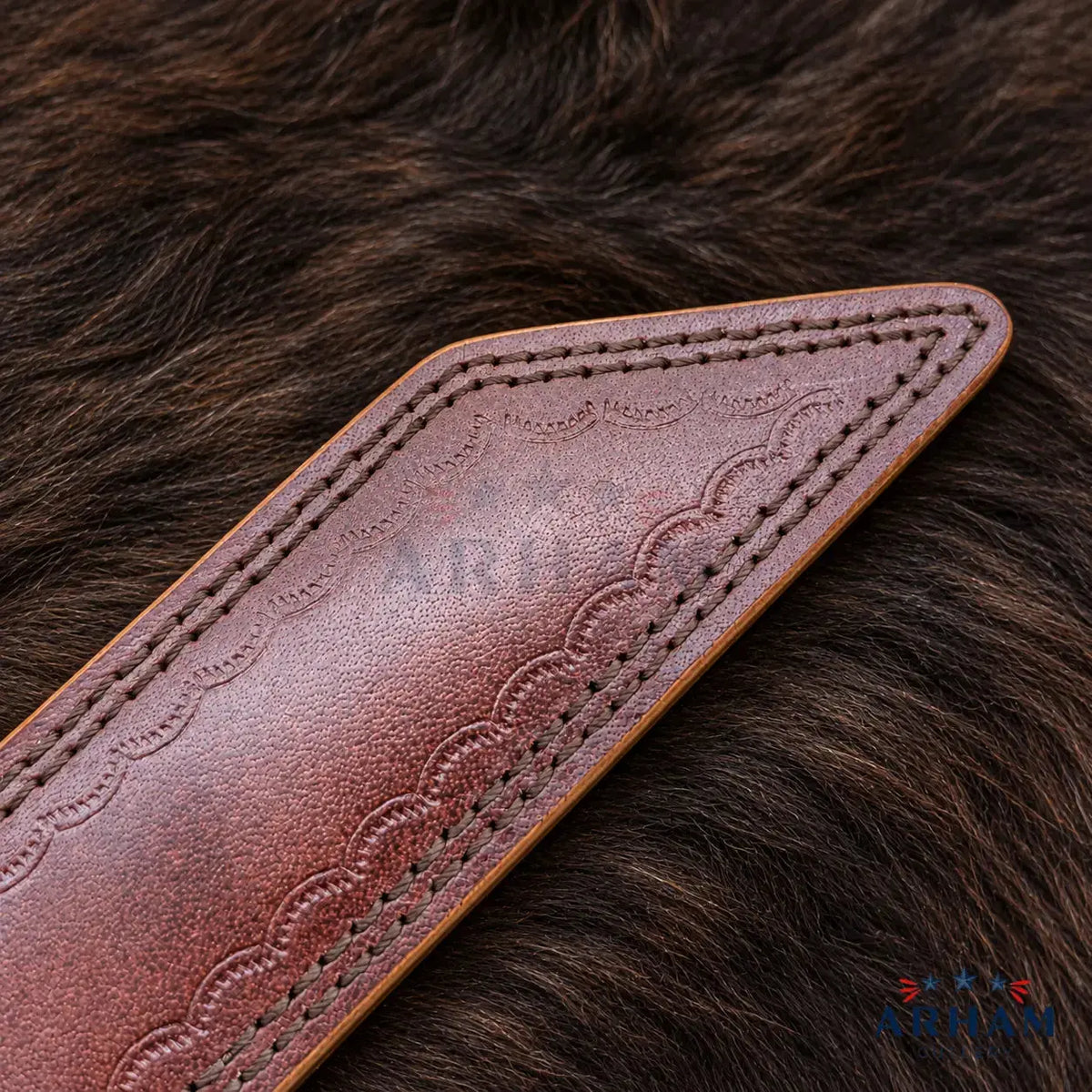 A close-up of a brown leather strap or belt section with scalloped tooling and contrast stitching, laid on a dark brown fur surface. A faint ARDUO watermark is visible across the leather, and an ARDUO logo appears in the bottom right corner.