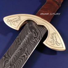 Cargar imagen en el visor de la galería, UlfSune Damascus Viking Sword with brass wolf guard, leather-wrapped handle, and back-carry red leather sheath – Arham Cutlery
